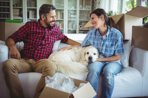 Couple sitting on sofa with their pet dog in their new house