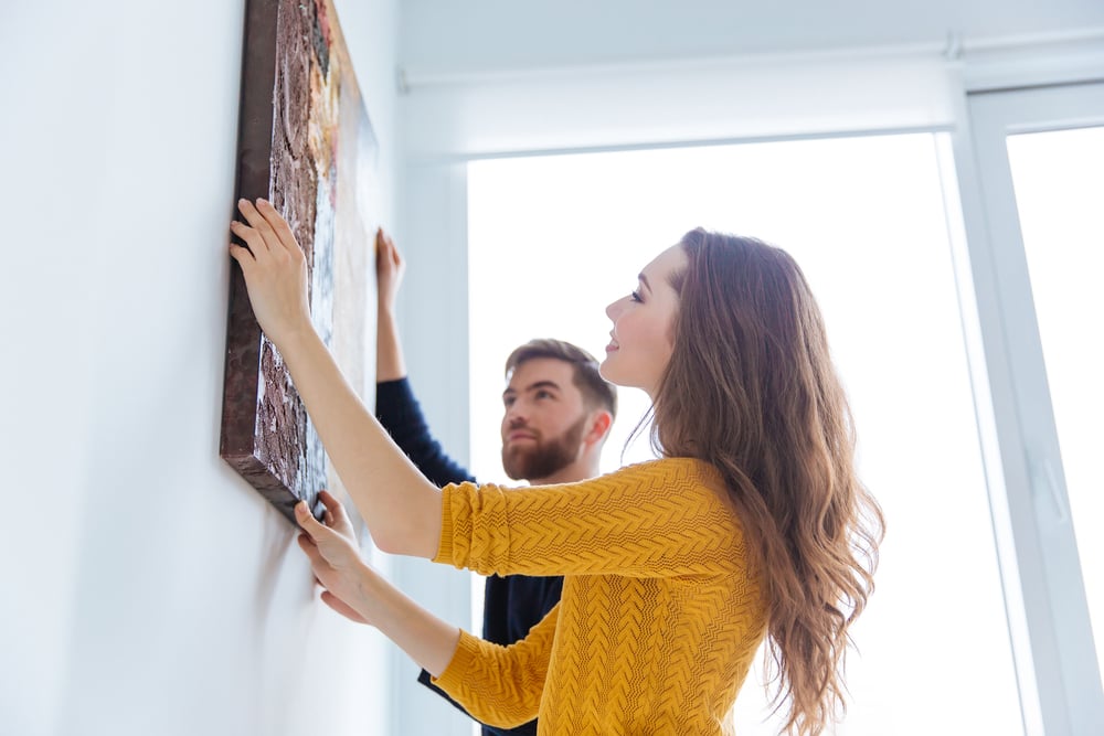 Happy couple hanging picture on the wall at home-1