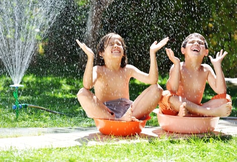 Happy kids playing and splashing with water sprinkler on summer grass yard