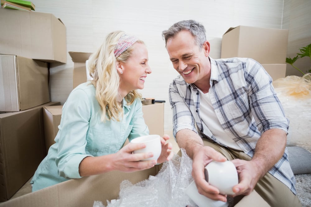 Smiling couple packing mug in a box at home